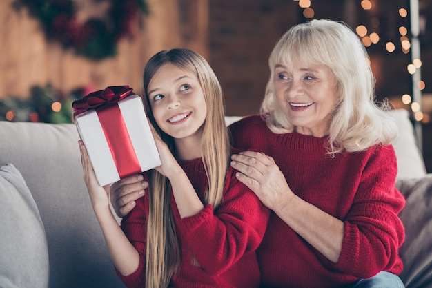 Closeup portrait of granny grandchild hold ribbon box at decorated interior house