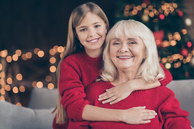 Closeup portrait of granny grandchild sit on divan cuddling at decorated loft style interior house