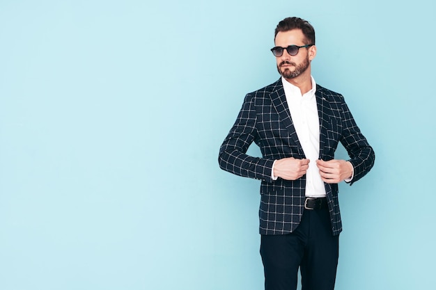 Closeup portrait of handsome confident stylish hipster lambersexual model Sexy modern man dressed in black elegant suit Fashion male posing in studio blue wall