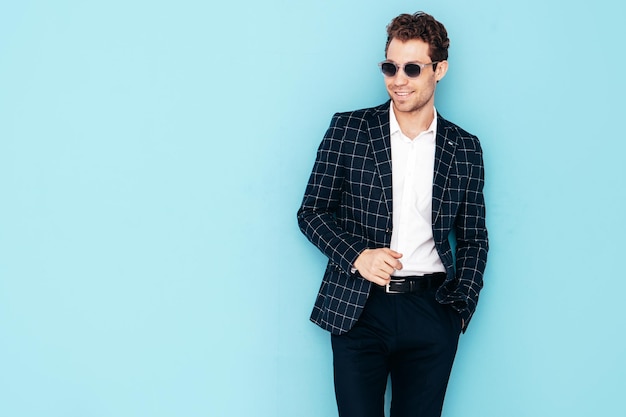 Closeup portrait of handsome confident stylish hipster lambersexual model Sexy modern man dressed in black elegant suit Fashion male posing in studio blue wall