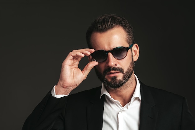 Closeup portrait of handsome confident stylish hipster lambersexual model Sexy modern man dressed in elegant black suit Fashion male posing in studio on dark background In sunglasses