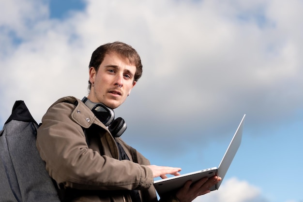 Closeup portrait of a handsome freelance man working on a laptop and looking to the camera with the sky as background.