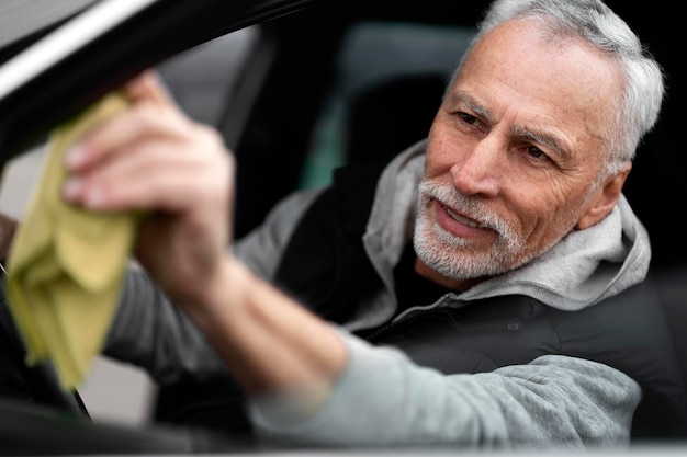 Closeup portrait of handsome positive whitebearded man driver wiping the car's side mirror