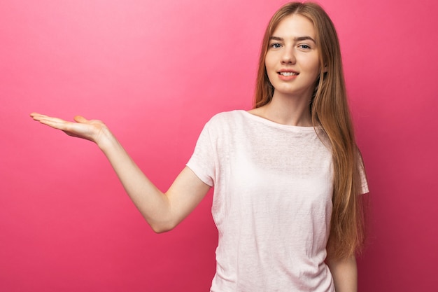 Closeup portrait of happy blonde woman showing the front finger to the side, stands on a pink wall