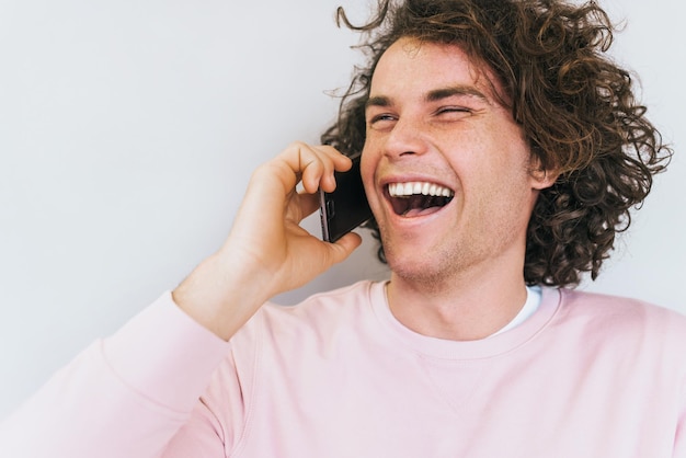 Closeup portrait of happy cheerful male with curly hair has communication with friend via mobile phone Handsome man smiling and laughing spreaking via smart phone People technology concept