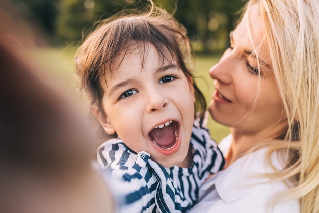 Closeup portrait of happy cute little girl looking to the camera embracing her mother in the park Loving mother and daughter spend time together in the park Motherhood and childhood People emotion