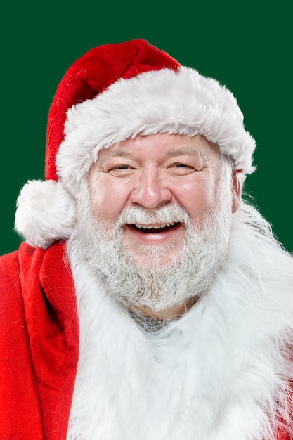 Closeup portrait of a happy laughing Santa Claus dressed in a red coat and a hat, isolated green background.