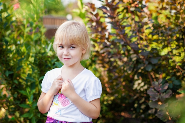 Closeup portrait of happy little blobde girl in elementary school age outdoors in green park