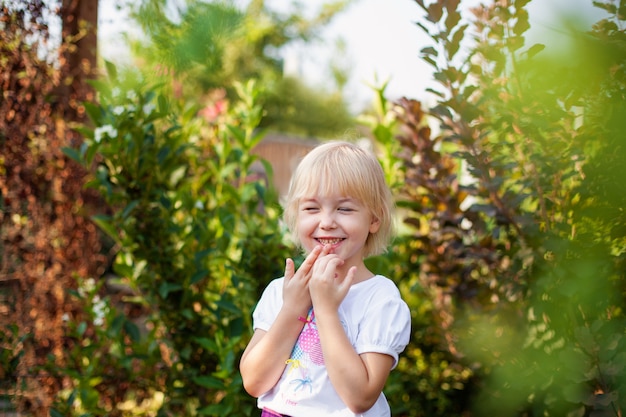 Closeup portrait of happy little blobde girl in elementary school age outdoors in green park