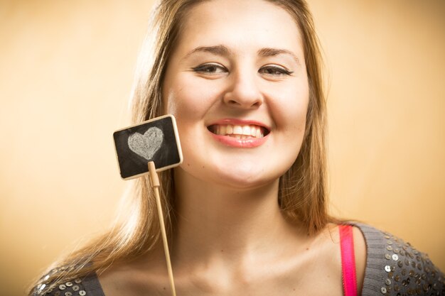 Foto ritratto del primo piano della donna sorridente felice che tiene la lavagna con cuore disegnato drawn