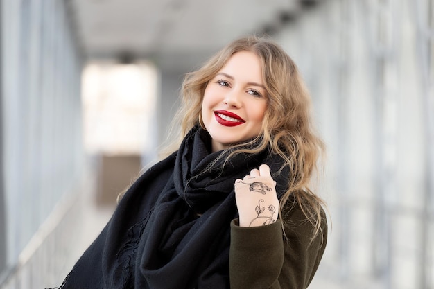 Closeup portrait of a happy young woman smiling Stylish fashion portrait woman Posing in the city Beautiful girl in autumn green coat and black scarf poses in an overhead pedestrian crossing