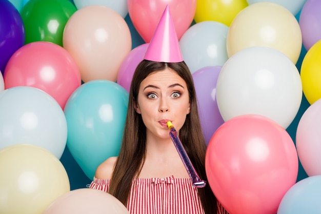 Closeup portrait of her she nice attractive lovely pretty amazed funny girlish cheerful cheery longhaired girl blowing festal whistle having fun among many colorful air balls