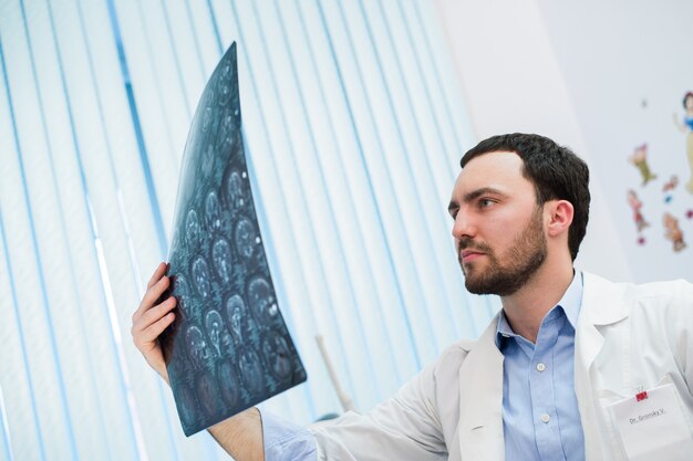 Closeup portrait of intellectual man healthcare personnel with white labcoat, looking at brain x-ray radiographic image