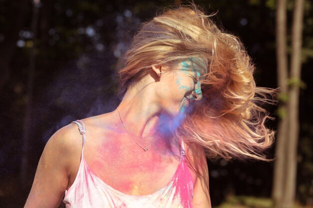 Closeup portrait of joyful blonde woman with fluttering hair in wind playing with powder Holi