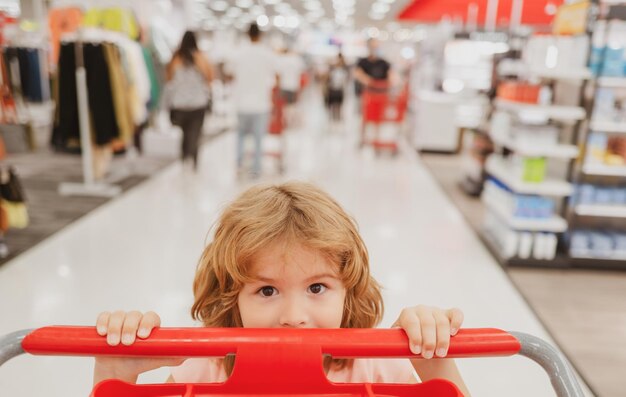 Photo closeup portrait of kid at grocery or supermarket with goods in shopping trolley