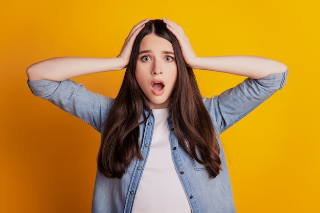 Closeup portrait of lady hands head open mouth staring isolated yellow wall background