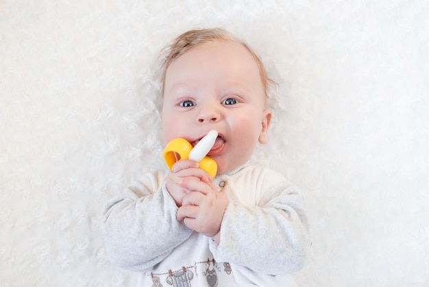 Closeup portrait little cute boy with big blue eyes with a toy in his hands, nibbles a banana teether toy