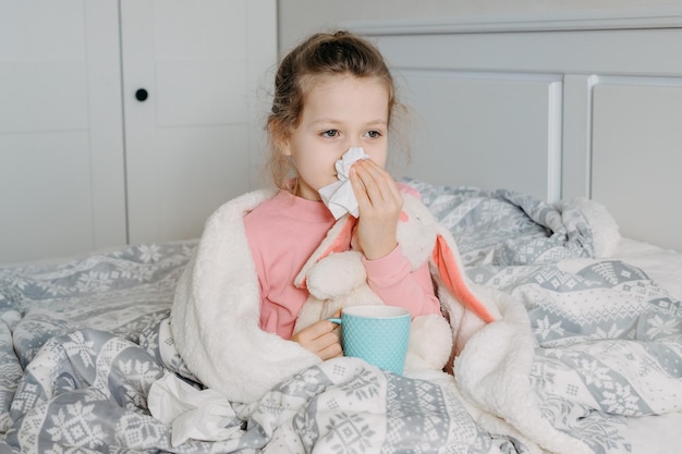 Closeup portrait of little sick girl child sneezes into paper tissue