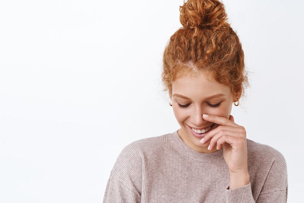 Closeup portrait lovely coquettish and elegant redhead woman showing sensuality comb hair in messy bun look down silly touching face as blushing from compliment stand white background happy