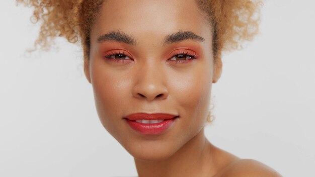 Closeup portrait of mixed rase woman with red makeup in studio smiling slightly and watching to the camera