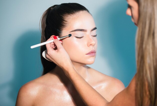 Closeup portrait of a model with bright makeup on a face makeup artist applies eye shadow hand of