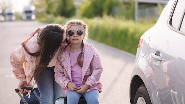 Closeup portrait of mom kiss her daughter in cheek during they waiting a trip Little girl sitting on her suitcase