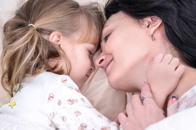 Closeup portrait of mother and daughter hugging in bed before going to bed