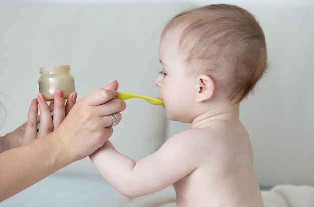 Ritratto del primo piano della madre che alimenta il suo bambino con purea di verdure alla camera da letto