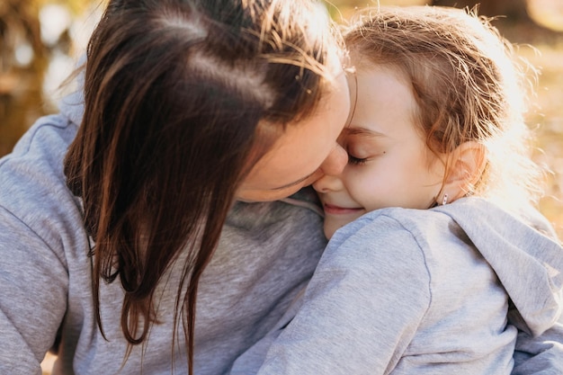 Closeup portrait of a mother kissing her daughter whom she holds in her arms outside in the park fam...