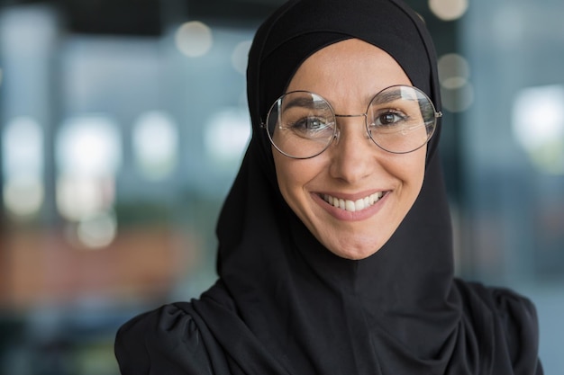 Ritratto del primo piano della donna d'affari musulmana in hijab che sorride e che esamina la lavoratrice della macchina fotografica dentro