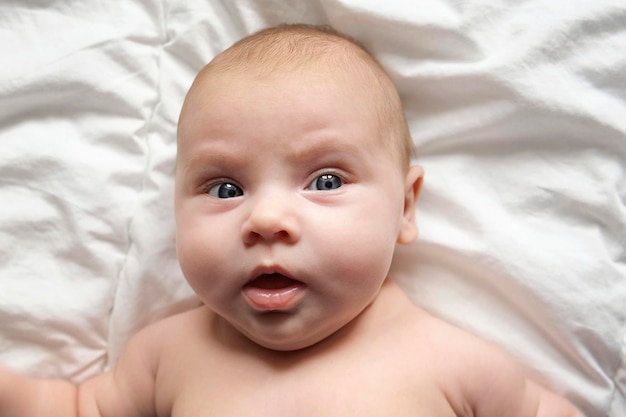 Closeup portrait of newborn baby on white blanket soft focus\
infant is lying yawning one two week age infant girl waking up on\
bed at home new life and growing up concept real people