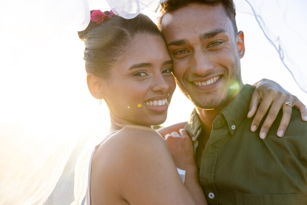 Closeup portrait of newlywed biracial couple embracing at beach against clear sky at sunset