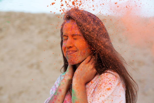 Фото Портрет крупного плана холодной женщины брюнет играя с взрывающейся оранжевой краской холи в пустыне. место для текста