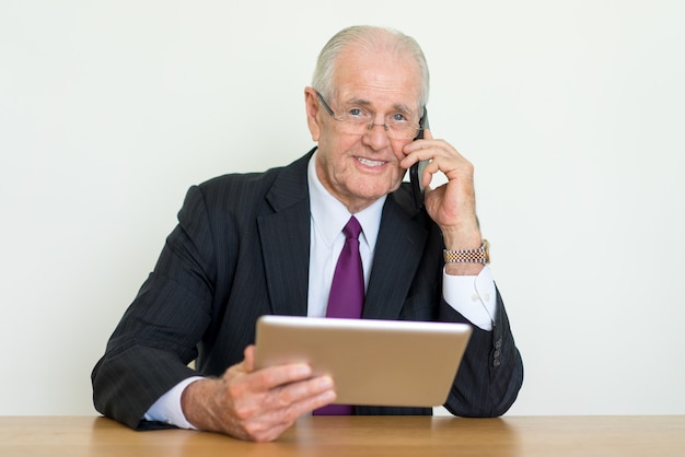 Макрофотография портрет улыбается старший деловой человек, говорить на смартфоне и с помощью планшета