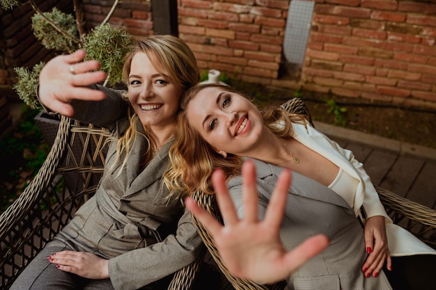 사진 엄격한 회색 정장을 입은 두 여자 친구의 클로즈업 초상화는 웃고 손으로 얼굴을 닫습니다.