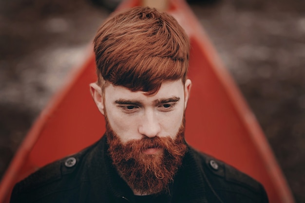 Closeup portrait of one handsome serious redhead man with long red beard in coat