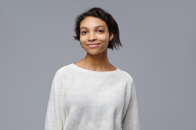 Крупным планом портрет позитивной африканской женщины в белом вязаном свитере на сером фоне
