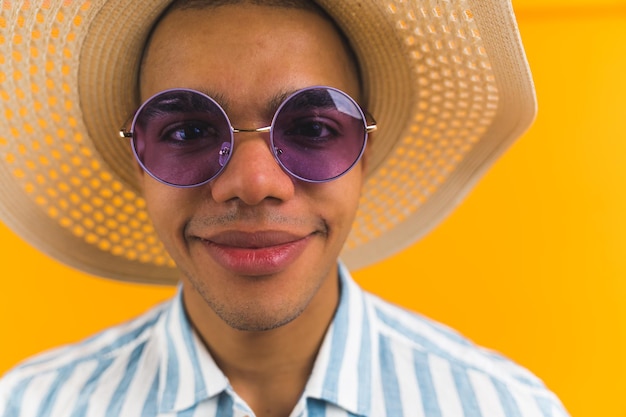 Closeup portrait of positive young adult man in violet sunglasses and straw hat looking at camera