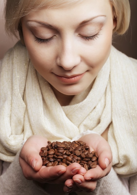 Closeup portrait of pretty blonde girl hold hot roasted coffee beans in hands