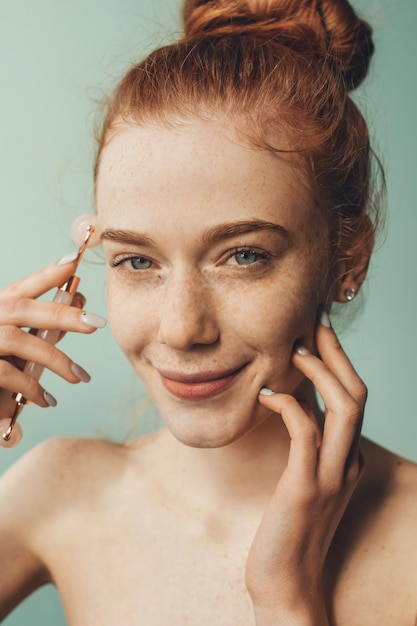 Closeup portrait of a red headed woman doing face massage with jade facial roller beauty face care f