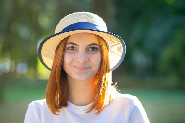 Closeup portrait of redhead hipster teenage girl in yellow hat smiling outdoors in sunny summer park.