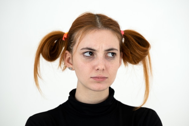 Closeup portrait of a sad redhead teenage girl with childish hairstyle looking offended isolated on white backround.