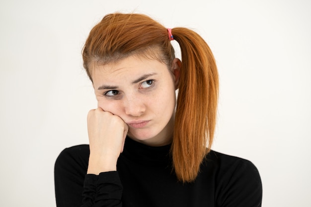 Closeup portrait of a sad redhead teenage girl with childish hairstyle looking offended isolated on white backround.