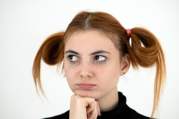 Closeup portrait of a sad redhead teenage girl with childish hairstyle looking offended.