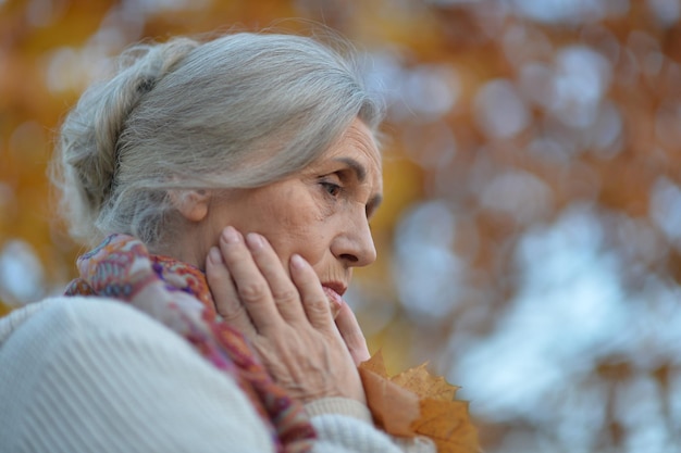 Closeup portrait of sad senior woman in autumn park