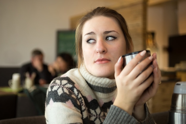 Closeup portrait of sad woman in sweater drinking coffee at cafe