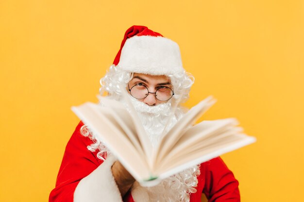 Closeup portrait of Santa Claus in the studio in front of the yellow wall holding a book