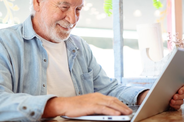 Фото Крупный портрет старшего бородатого мужчины, использующего ноутбук, пишущего на клавиатуре, сидящего в помещении и просматривающего сеть.