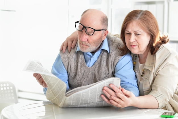 Closeup portrait of a senior couple with newspaper at home