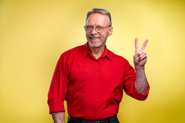 Closeup portrait of senior smiling business man holding up
peace victory two sign isolated on yellow background positive
emotion facial expressions symbols attitude communication life
success